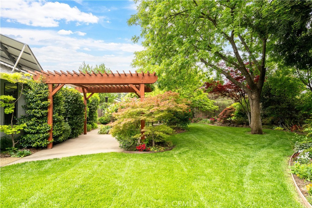 Landscaped backyard with a wooden pergola, paved walkway, broad lawn, and mature trees.