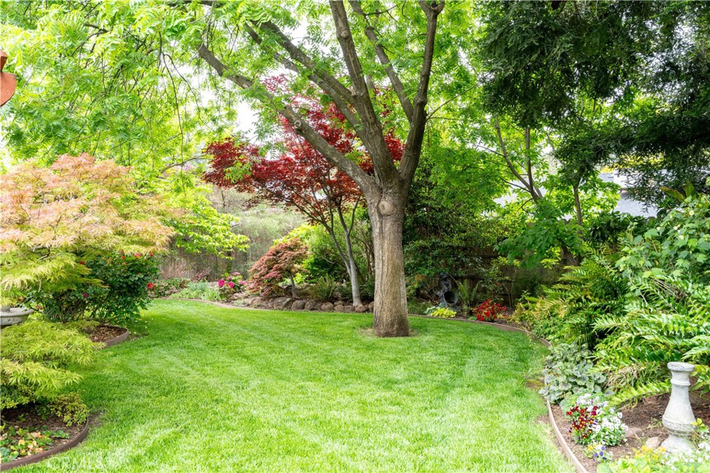 Landscaped backyard with a broad lawn, mature trees, and colorful garden beds.