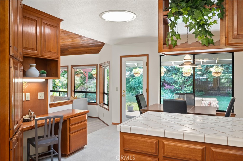 Kitchen with warm wood cabinetry, a tiled island, and large windows overlooking a green backyard.