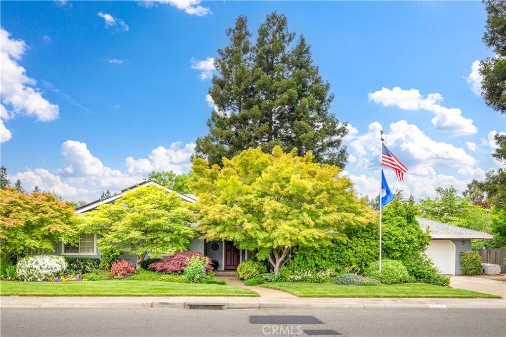 Single-story home with lush landscaping, mature trees, an attached garage, and flags by the lawn.