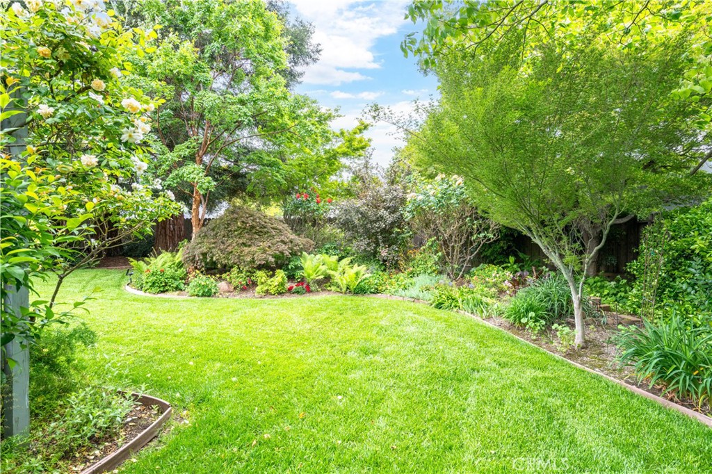 Landscaped backyard with a broad lawn, flowering garden beds, and mature shade trees.