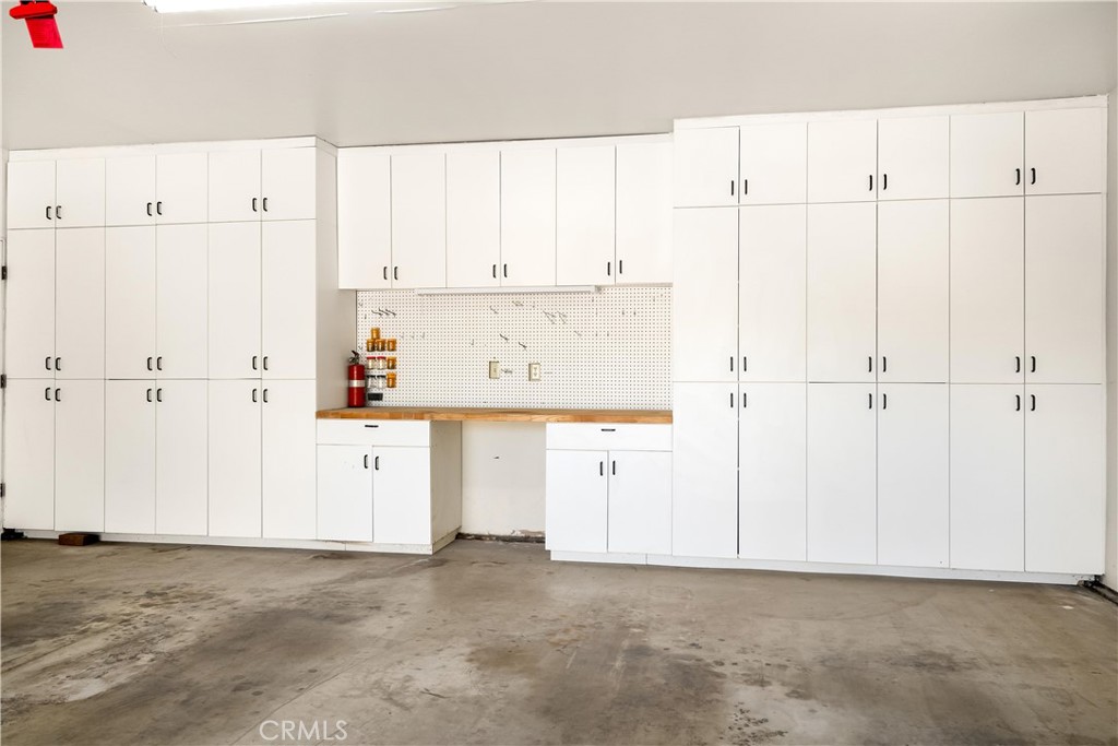 Garage with extensive white built-in cabinets, a wooden workbench, pegboard, and concrete floor.