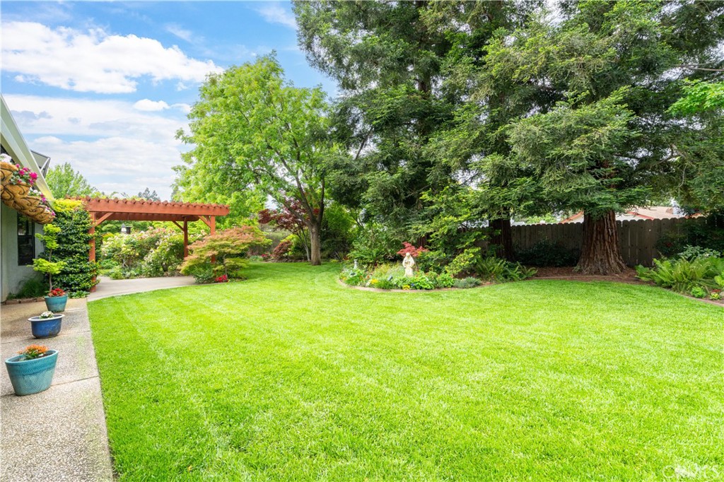 Landscaped backyard with a wide lawn, mature trees, flower beds, and a red wooden pergola.