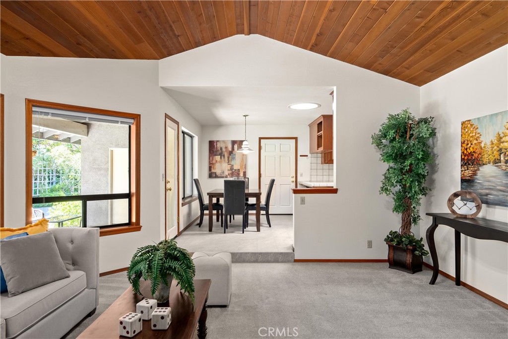Living room with vaulted wood ceiling, gray carpet, and an open view into the dining area.