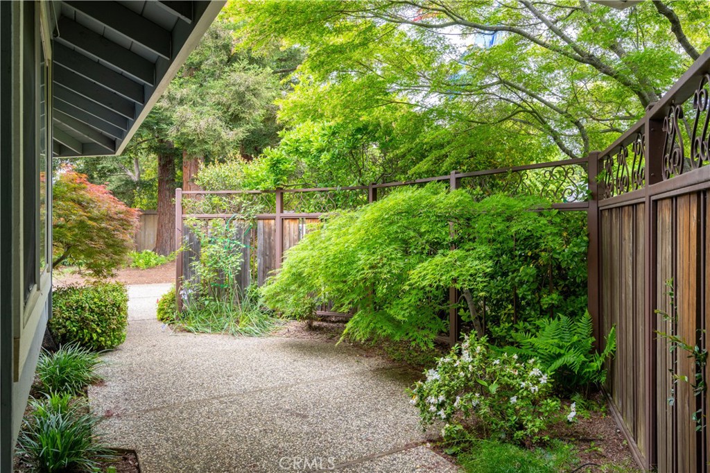 Garden walkway beside the house, bordered by lush shrubs and a decorative wooden fence.