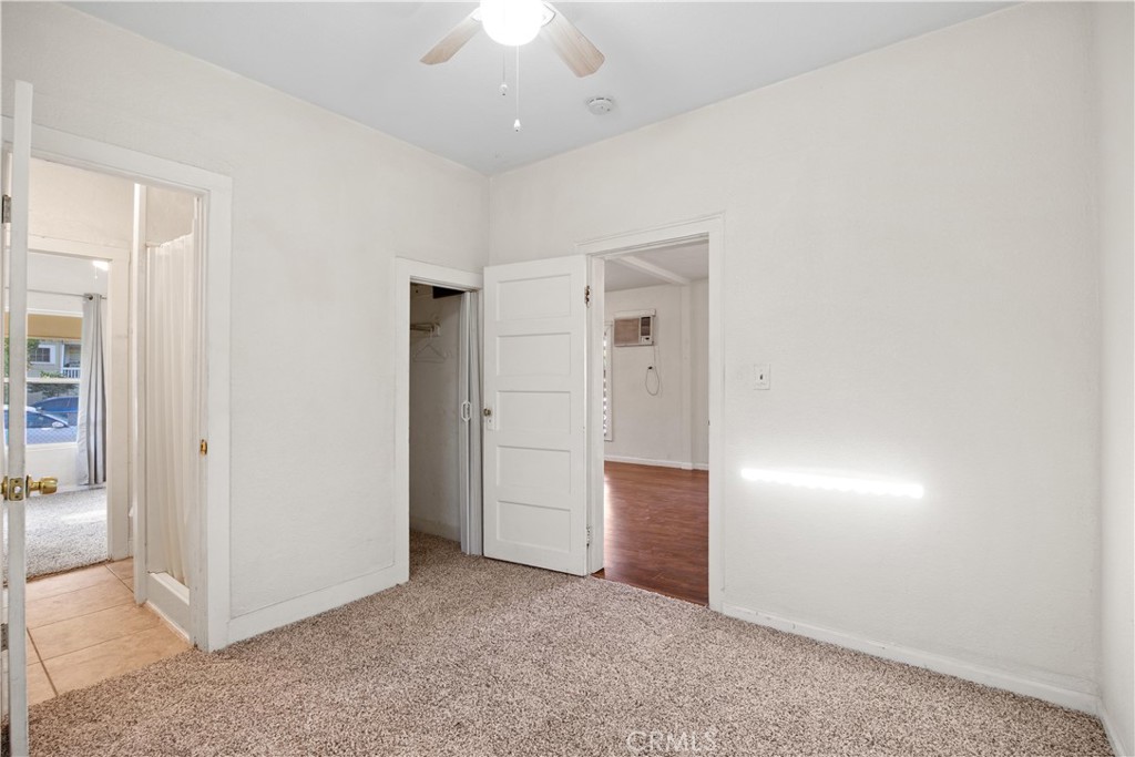 Empty bedroom with beige carpet, a ceiling fan, and an open closet.