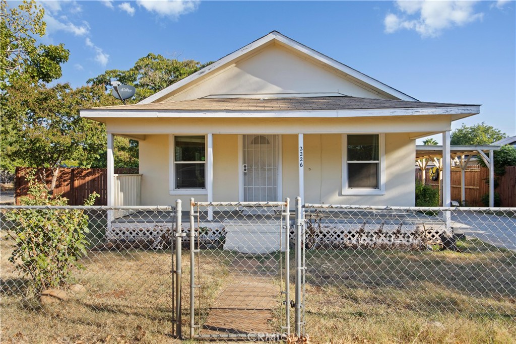 Cream-colored single-story house with a covered porch behind a chain-link fence.
