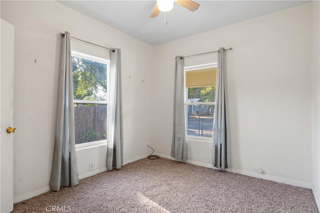 Empty bedroom with beige carpet, two curtained windows, and a ceiling fan.