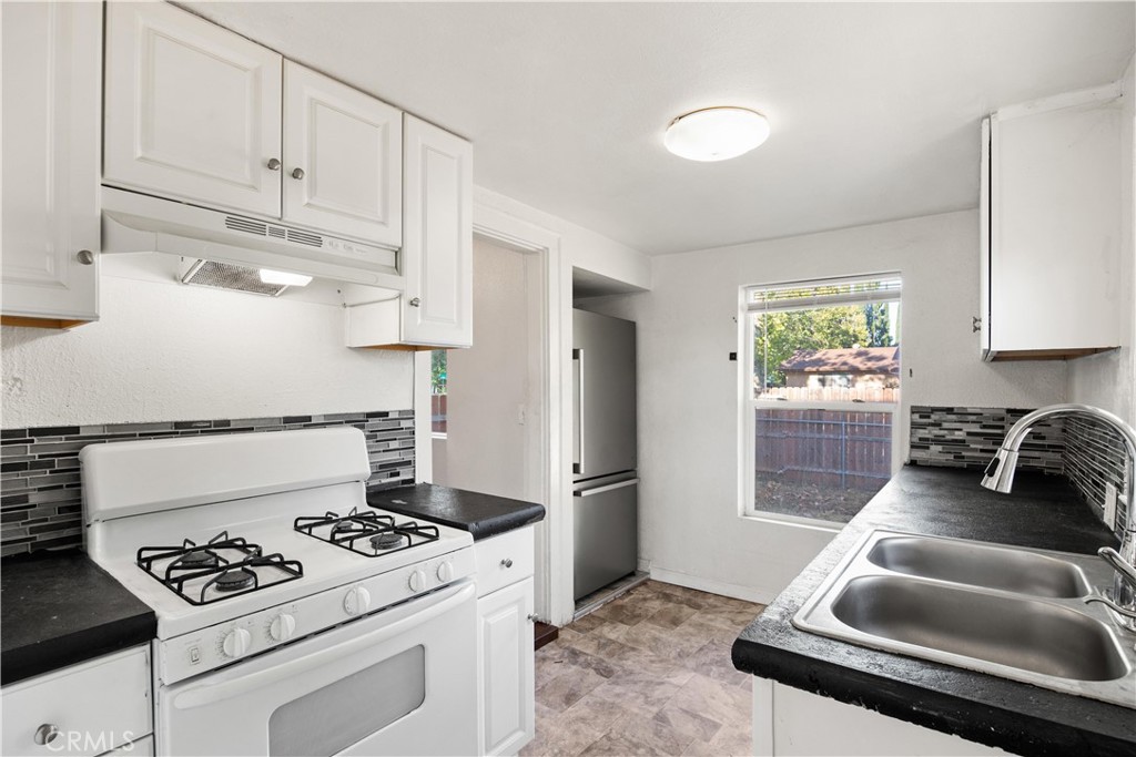 Kitchen with white cabinets, black countertops, gas range, and a double sink beside a window.