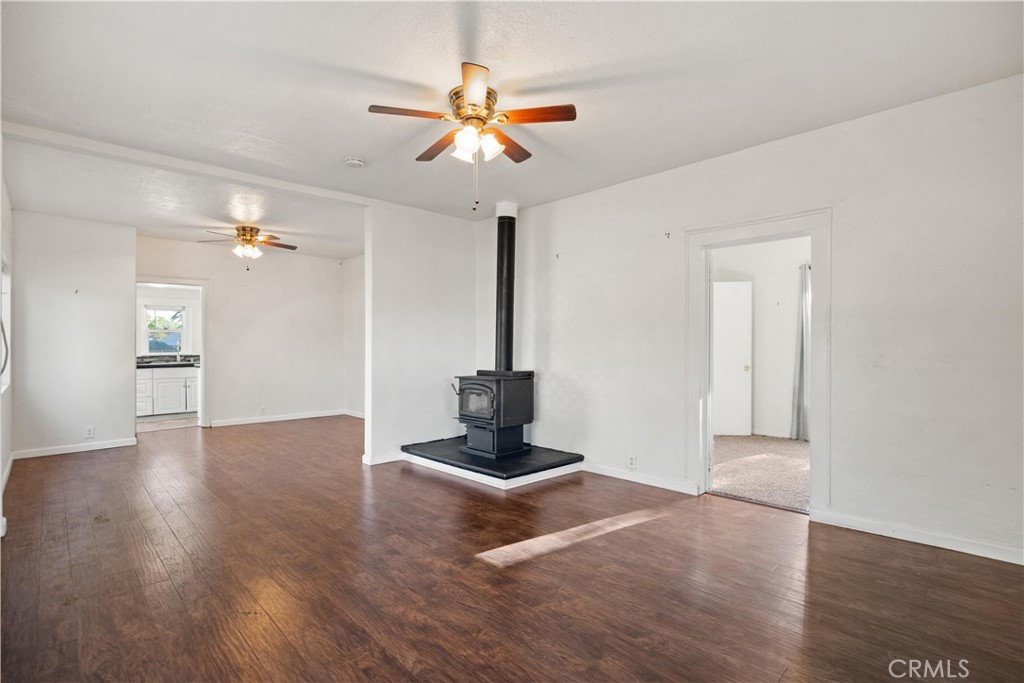 Empty living room with dark wood-look floors, ceiling fans, and a black wood-burning stove.