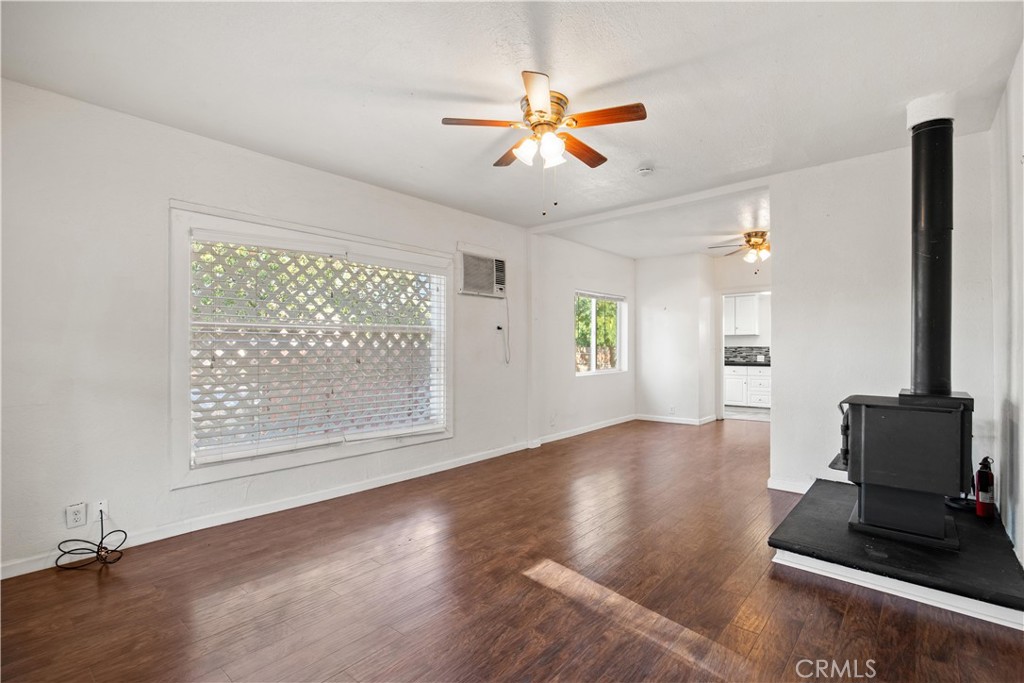 Unfurnished living room with wood-look floors, a large window, ceiling fans, and a black wood stove.