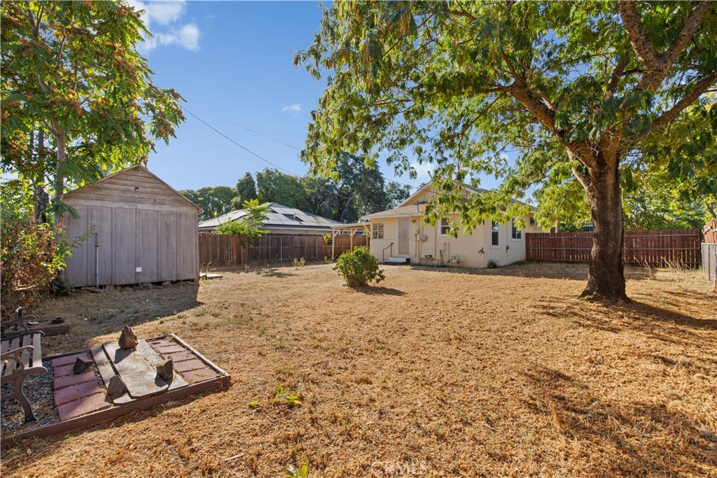 Backyard with a wooden shed, dry lawn, mature shade trees, and a small paved patio.