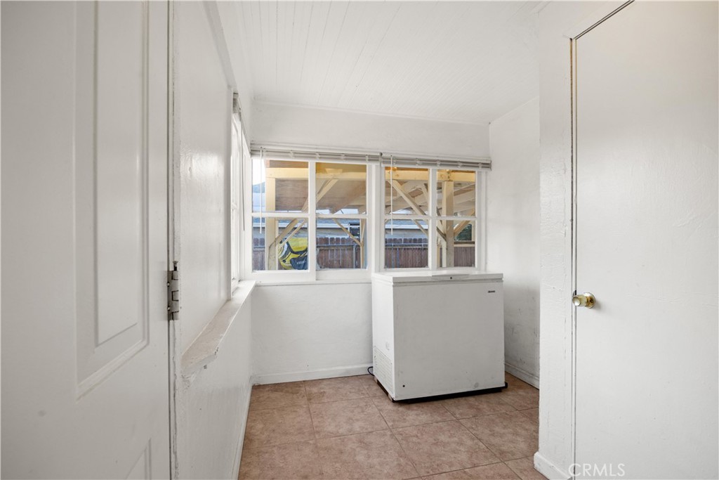 Utility room with a chest freezer, tan tile floor, and windows overlooking a covered structure.