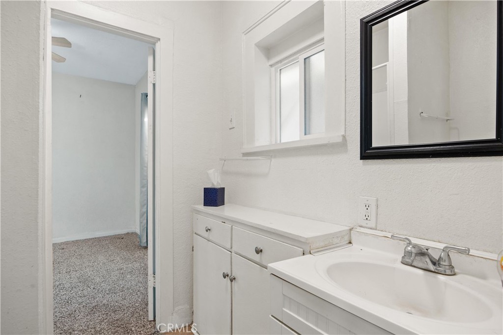 Bathroom with white vanity cabinets, a sink, black-framed mirror, and window.