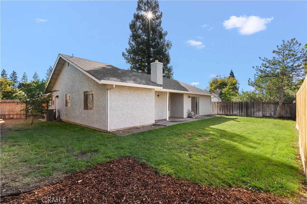 Rear of a single-story home with a broad lawn, fenced yard, and covered patio.