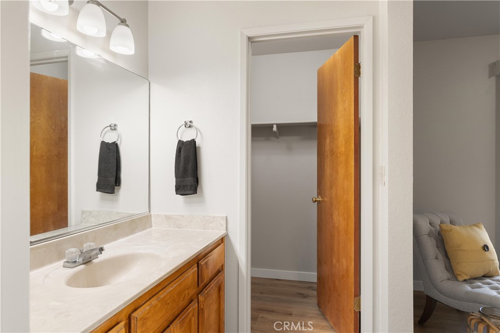 Bathroom with a long stone vanity and mirror beside an open closet doorway.