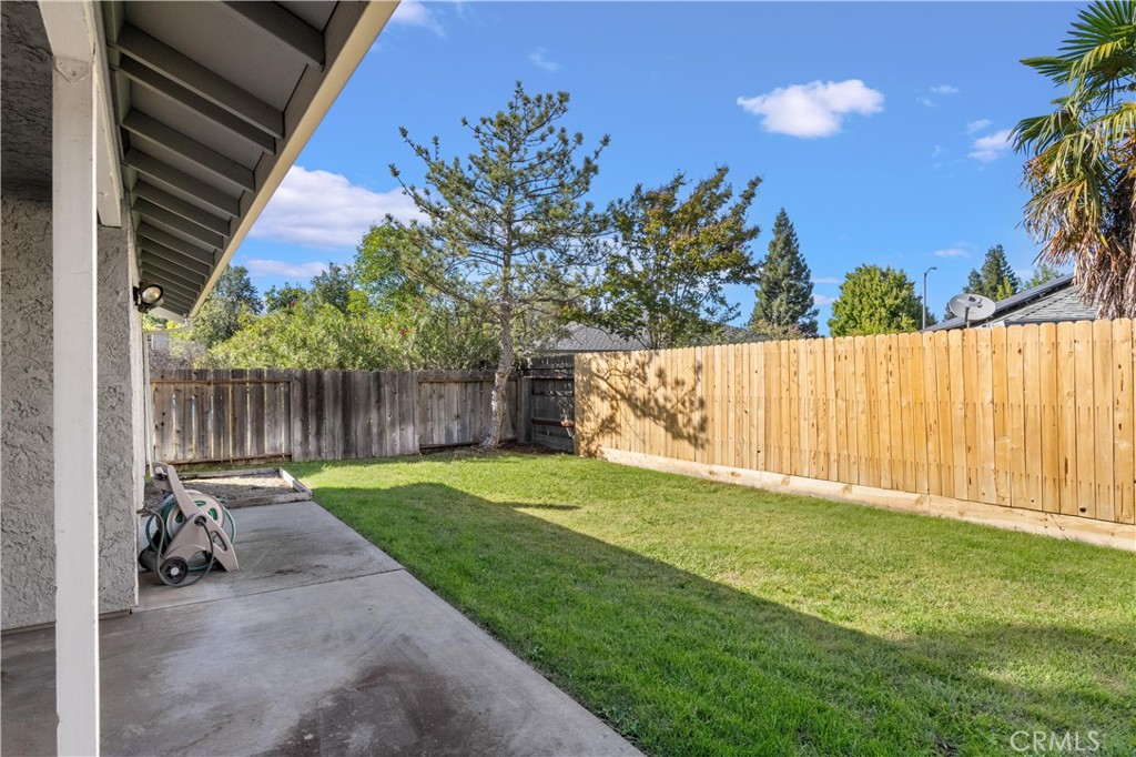 Backyard with a grassy lawn, covered concrete patio, mature trees, and wooden privacy fence.