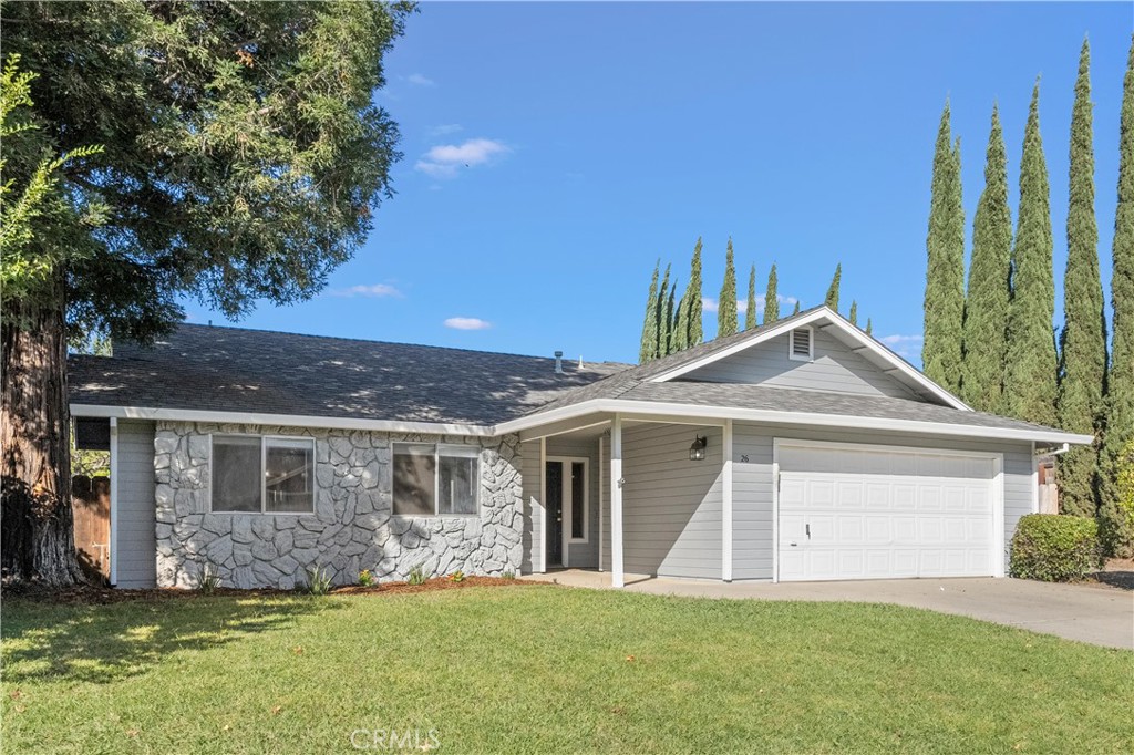 Single-story gray house with a stone facade, white double garage, and tall cypress trees.