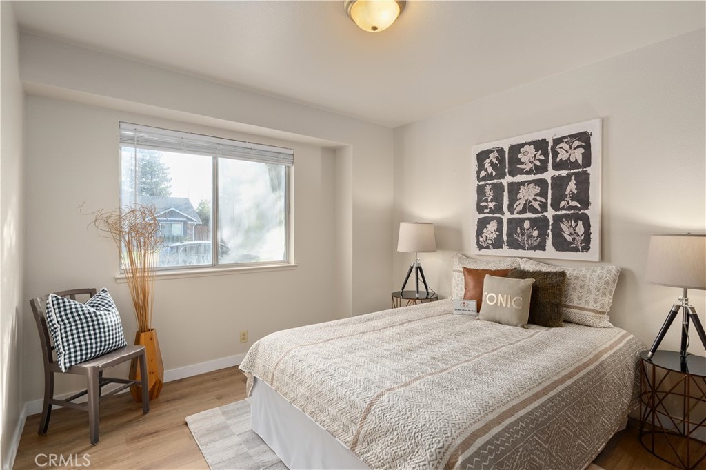 Staged bedroom with a large patterned bed, botanical wall art, and a window with blinds.