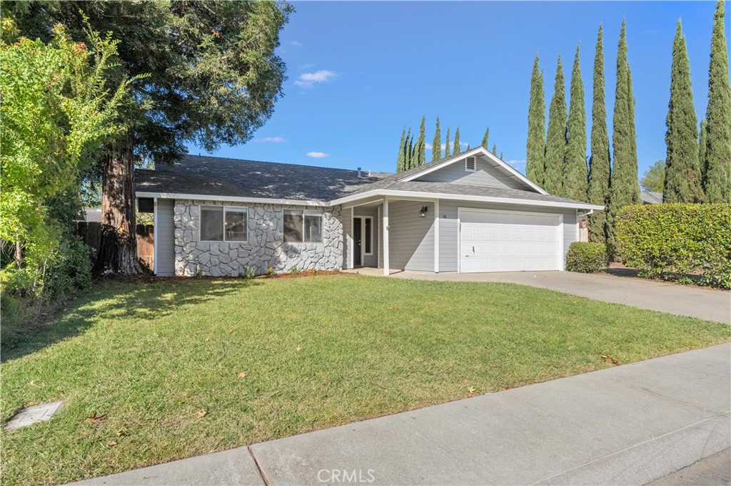 Single-story home with stone façade, white garage door, front lawn, and tall cypress trees.