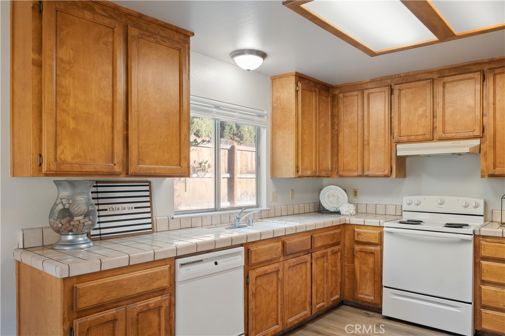 Kitchen with honey-toned wood cabinets, tiled counters, and white appliances.
