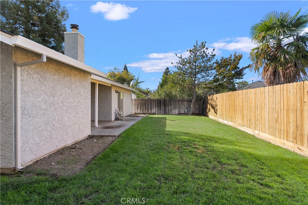 Backyard lawn beside a covered patio, enclosed by a tall wooden fence.