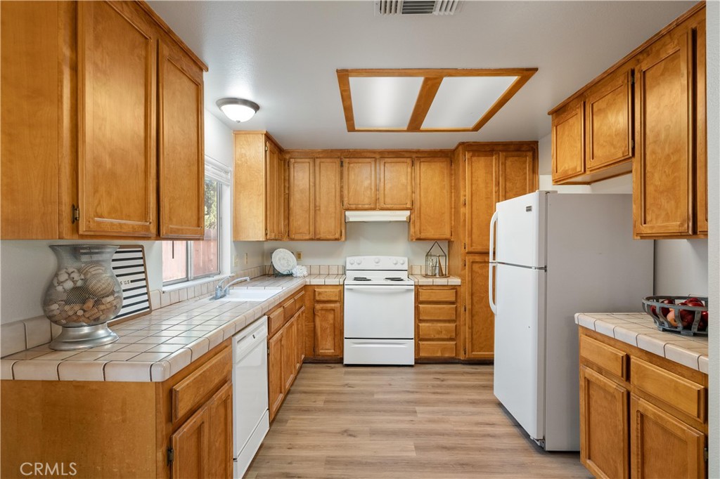 Kitchen with honey-toned wood cabinets, tiled counters, and white appliances.