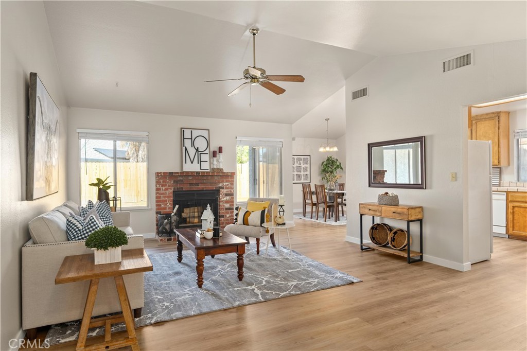 Staged living room with a brick fireplace, vaulted ceiling, and adjoining dining area.