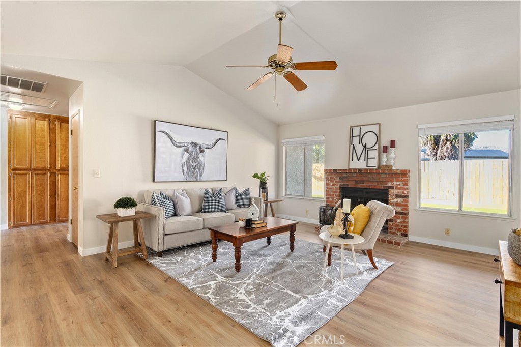 Staged living room with a brick fireplace, light sofa, patterned rug, and large windows.