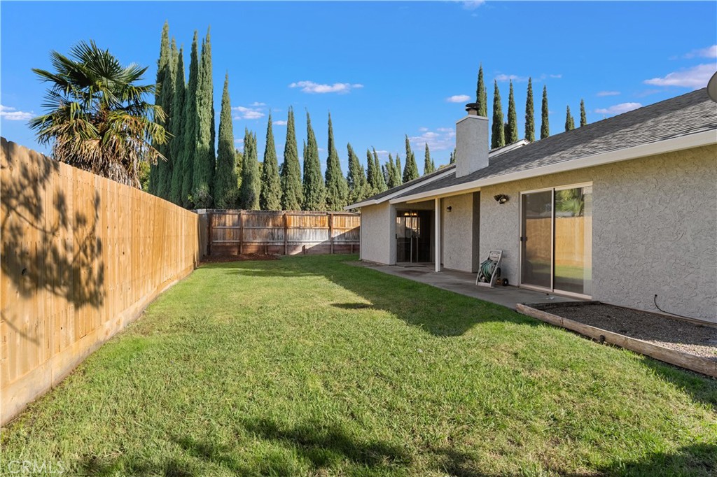 Backyard with a broad lawn, wooden fencing, covered patio, and sliding glass doors.