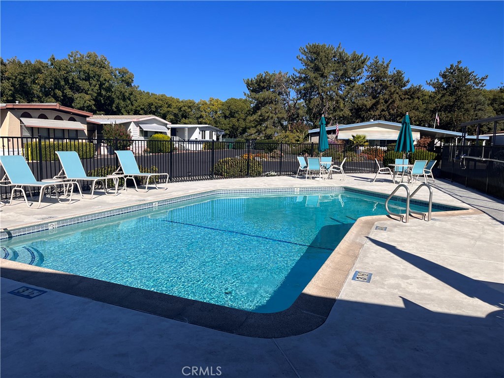 Community swimming pool with lounge chairs, patio tables, and teal umbrellas along the deck.