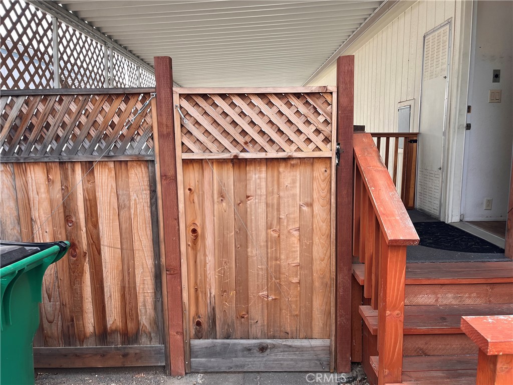 Covered entry with wooden steps and railing beside a tall lattice-topped privacy fence.