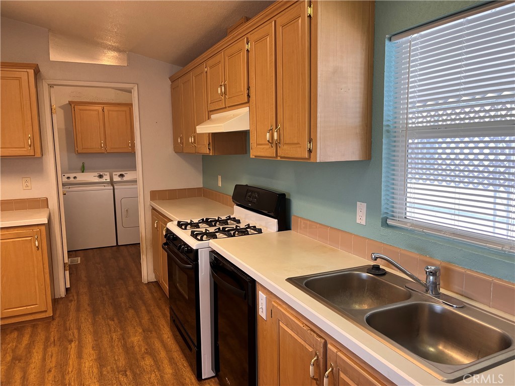 Kitchen with wood cabinets, a gas range, double sink, and washer and dryer in the adjoining laundry area.