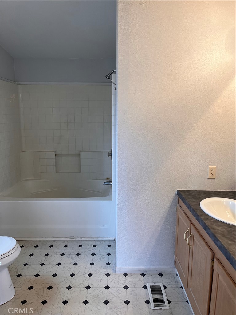 Bathroom with tiled tub and shower, wood vanity, and black-diamond patterned floor.