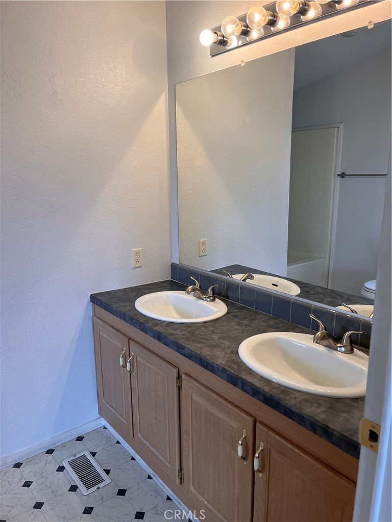 Bathroom with a double-sink vanity, dark countertop, wood cabinets, and patterned tile floor.