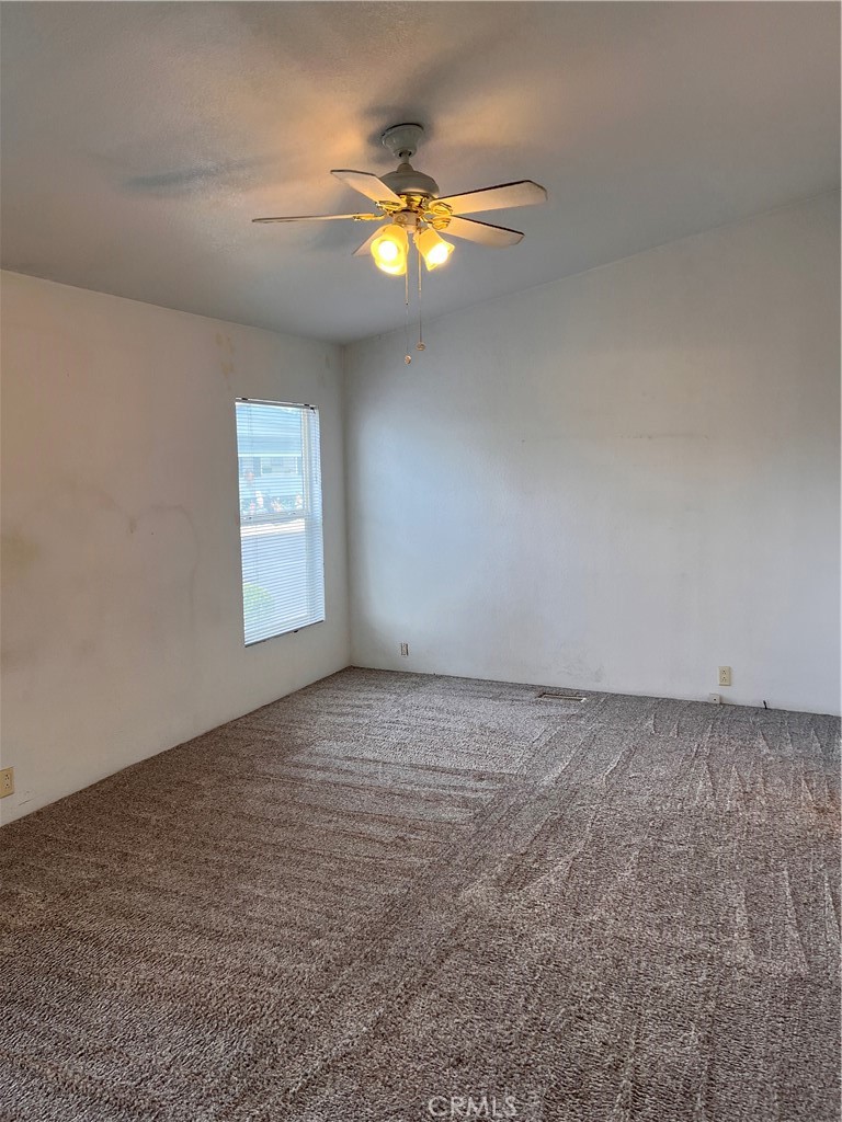 Empty bedroom with beige carpet, a window with blinds, and a lit ceiling fan.