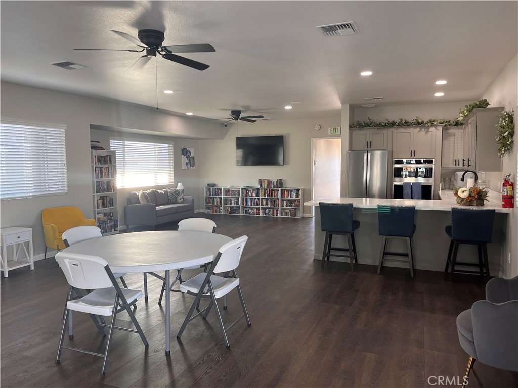 Furnished community room with bookshelves, lounge seating, a dining table, and a kitchen island.