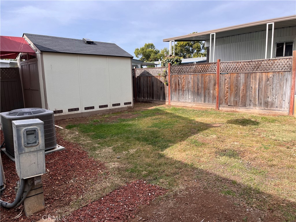 Fenced side yard with a small shed, patchy lawn, and outdoor air-conditioning equipment.