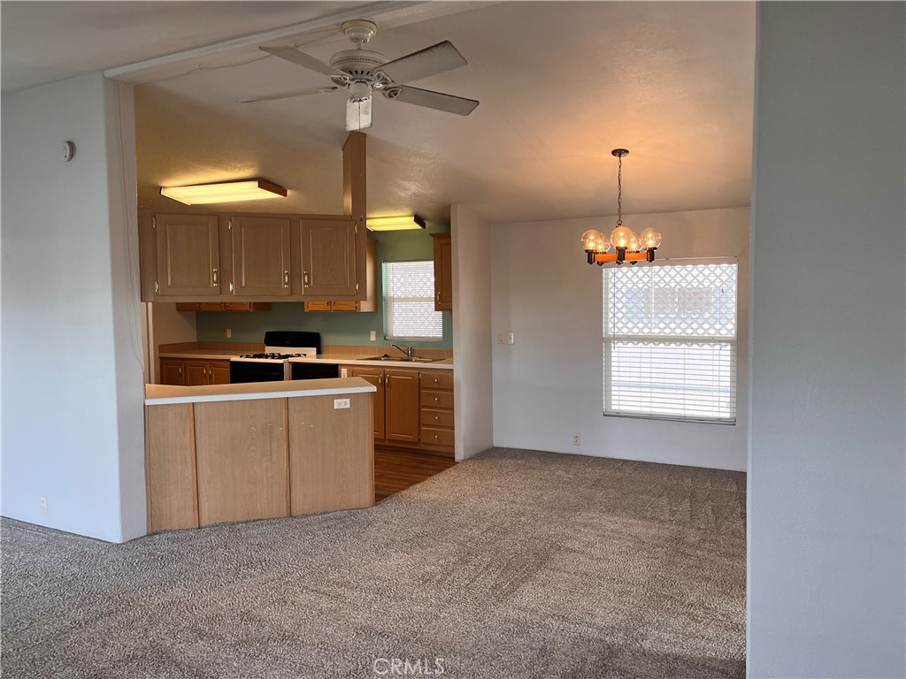 Open-plan kitchen and living area with wood-tone cabinets, a peninsula counter, and carpeted floor.
