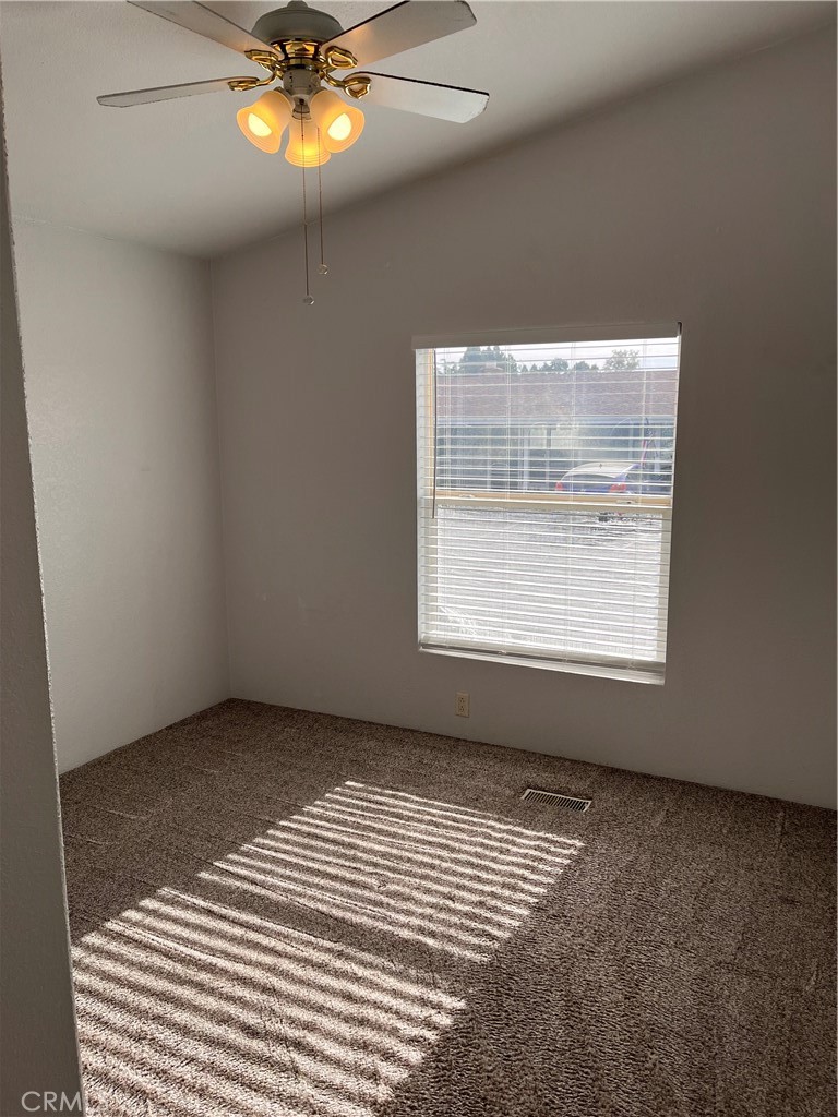 Empty carpeted room with a ceiling fan and sunlight striped across the floor through window blinds.