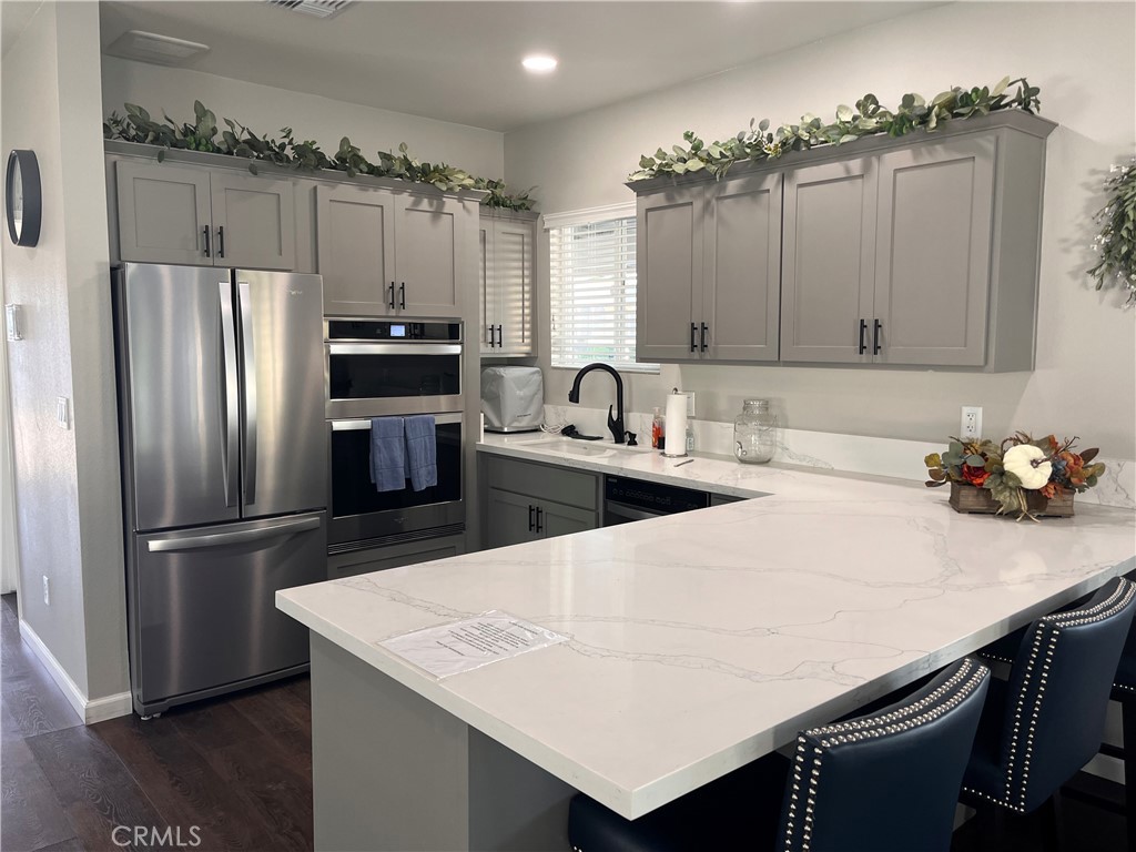 Kitchen with gray cabinets, stainless steel appliances, and a large veined-stone island with dark barstools.