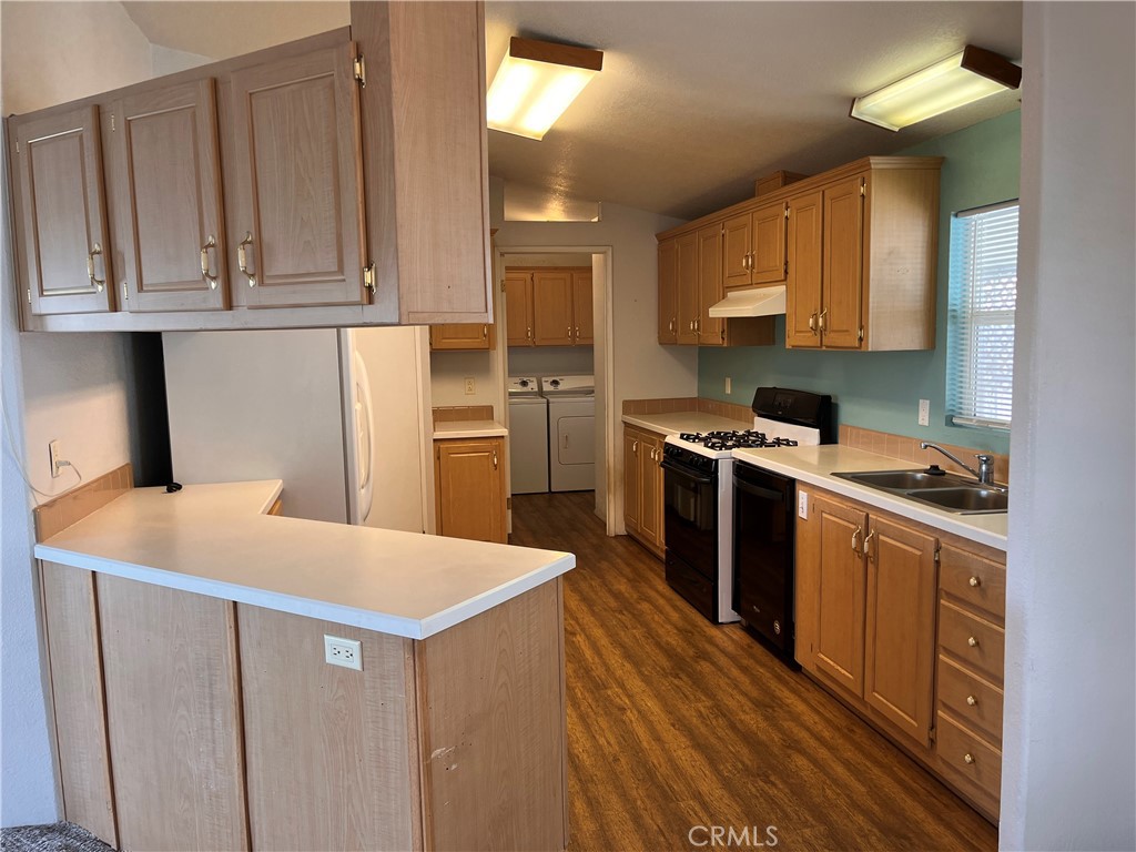 Kitchen with wood cabinetry, peninsula counter, gas range, and adjoining laundry appliances.