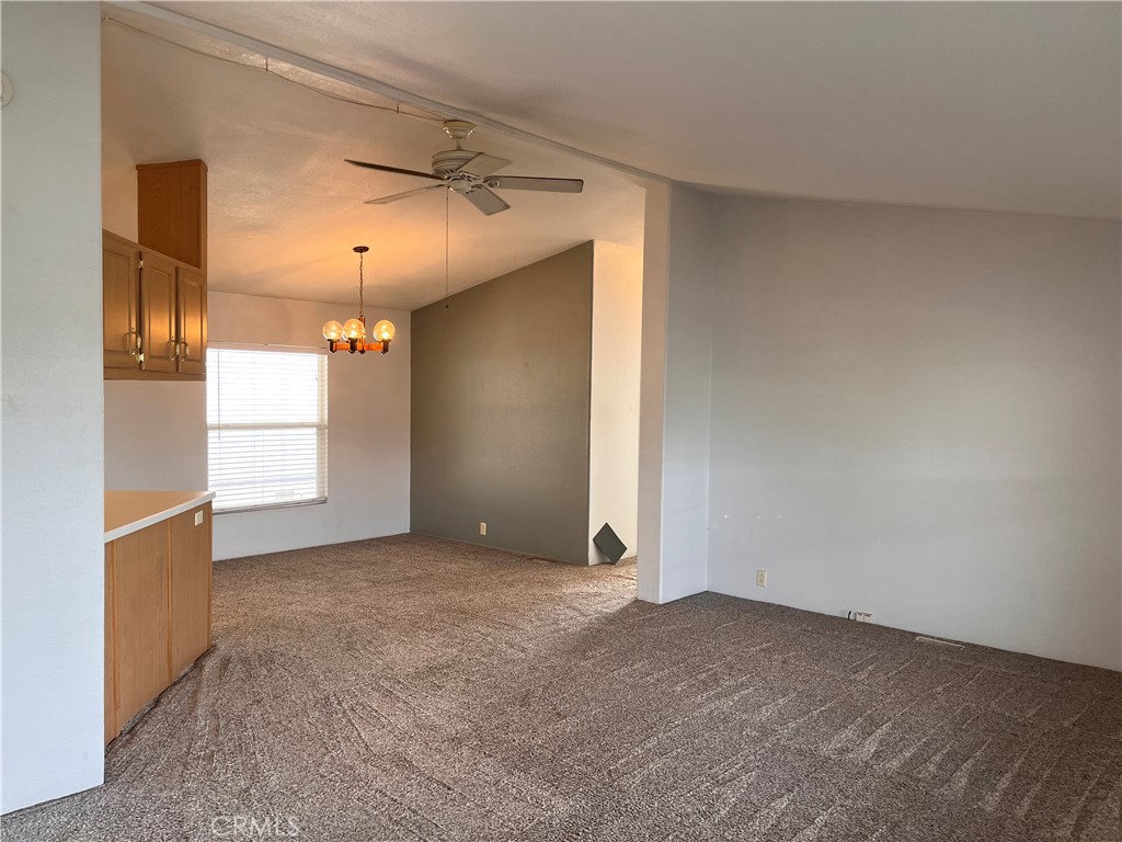 Empty carpeted living and dining area with a ceiling fan, chandelier, and wood cabinetry.