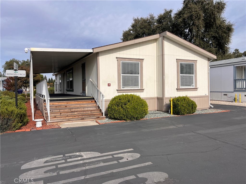 Cream manufactured home with a covered porch, wooden steps, and two front windows.