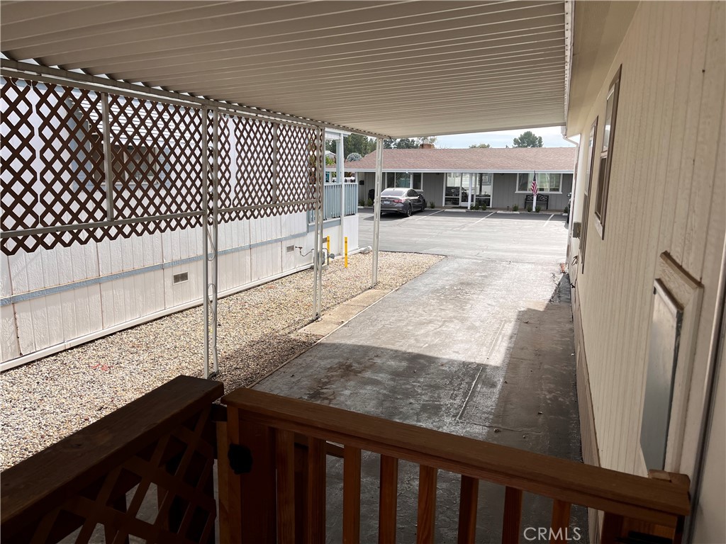 Covered walkway and driveway beside a residence, with lattice screening and a parking area.