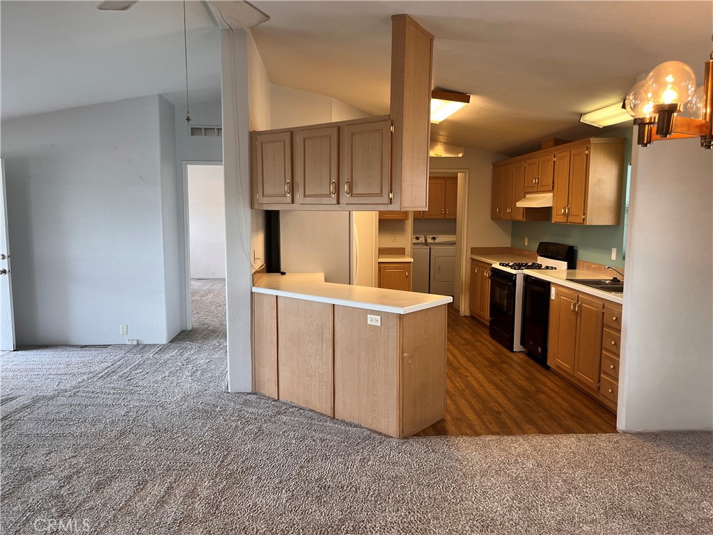 Open kitchen with a peninsula, light wood cabinets, black appliances, and laundry area beyond.
