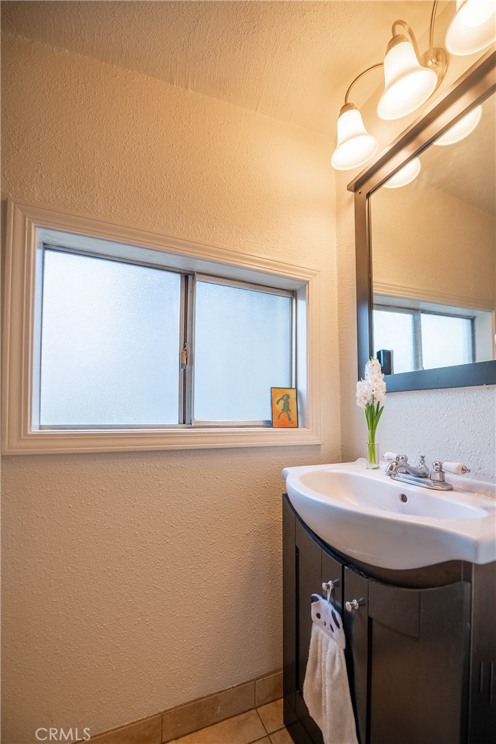 Bathroom vanity with a white sink, large mirror, and frosted window.