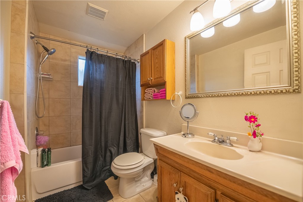 Bathroom with tiled tub and shower, dark curtain, and wood vanity with framed mirror.