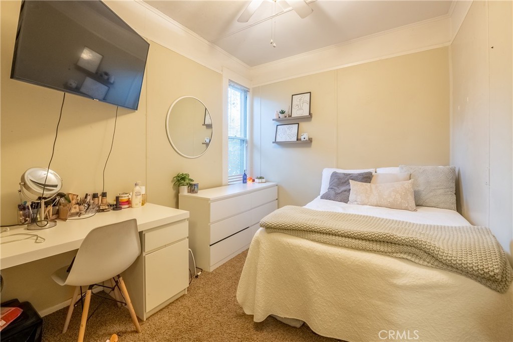 Bedroom with white bedding, a textured throw, and a desk beneath a wall-mounted television.