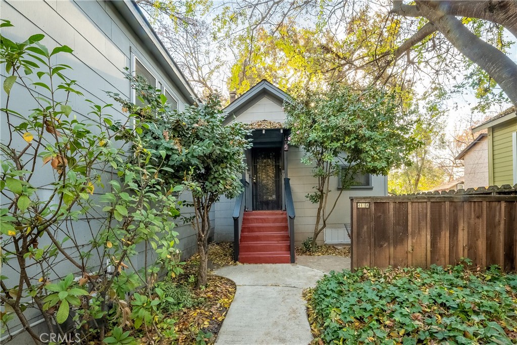Gray home entrance with red steps, a screened door, and a leafy walkway.